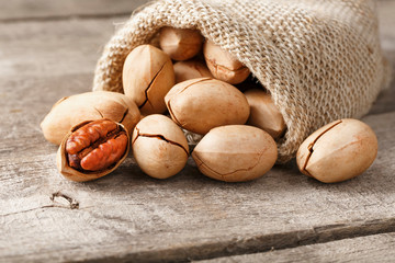 Pecans spill out of a bag on a wooden table, close-up. Peeled, in a shell.