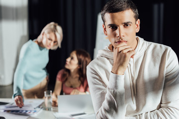 selective focus of pensive art director looking at camera near coworkers