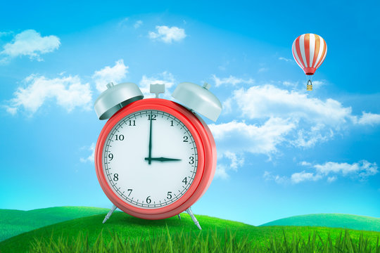 3d rendering of red retro alarm clock showing 3 o'clock standing on green grass under blue sky with hot air balloon in distance.