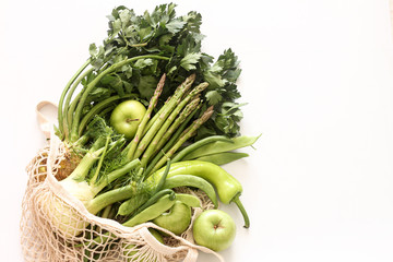 Green vegetables and fruits in  string bag on white background.