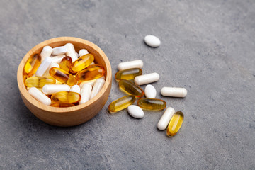 Assortment scattered pharmaceutical medicine tablets, pills, drugs in wooden bowl on gray...