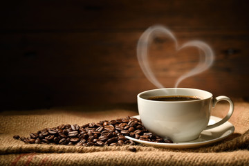 Cup of coffee with heart shape smoke and coffee beans on burlap sack on old wooden background