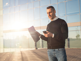 Business man standing in front of glass office building, using his mobile phone hands free 