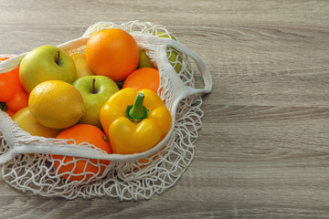 Net bag with vegetables and fruits on wooden table. Space for text