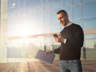 Business man standing in front of glass office building, using his mobile phone hands free 