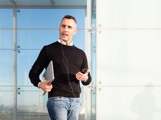Business man standing in front of glass office building, using his mobile phone hands free 