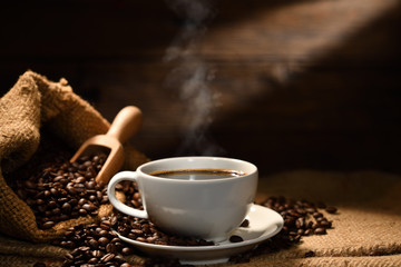 Cup of coffee with smoke and coffee beans on burlap sack on old wooden background