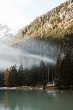 Wooden house on stilts and boats on nebulous lake with reflection of powerful Dolomites mountains at Italy