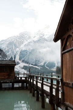 Wooden house on stilts and boats on nebulous lake with reflection of powerful Dolomites mountains at Italy