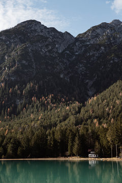 Wooden house on stilts and boats on nebulous lake with reflection of powerful Dolomites mountains at Italy