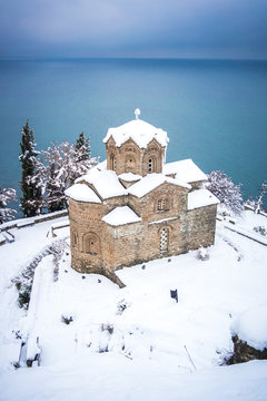 Ancient Orthodox church covered with snow located on coast located on shore of peaceful Ohrid lake on winter day in North Macedonia