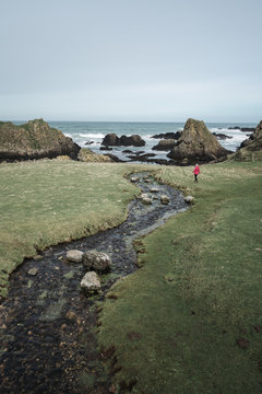 From above anonymous woman enjoying amazing scenic landscape of Northern Ireland during travel while walking near fast shallow river flowing to waters of rocky shore