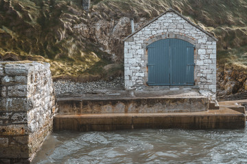 Ancient stone building with doors on picturesque pier of Ballintoy harbour on rocks background