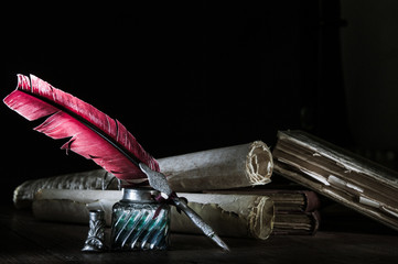 Quill pen and a rolled papyrus sheet on a wooden table with old books, high contrast