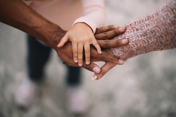From above crop faceless diverse parents and child joining hands together outdoors at daytime