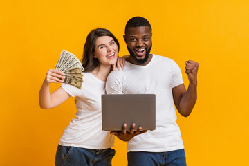 Overjoyed interracial couple with dollar cash and laptop celebrating win together