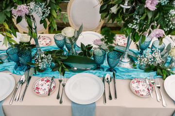 From above of wedding table decorated with blue and beige cloth and flowers bouquets in tall vases and served with porcelain plates and blue glasses