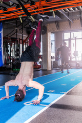 Fototapeta na wymiar Athlete walking on his hands standing upside down in gym. Man doing push ups on his hands. Crossfit training.