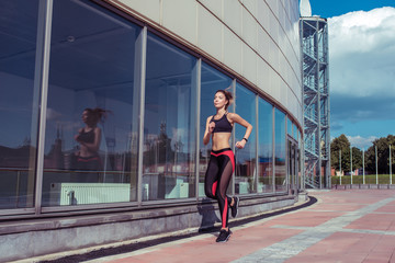 Fototapeta na wymiar Beautiful girl runs in summer in city, jogging in early morning and afternoon, fitness training in fresh air. Free space for copy text. Sportswear, tanned figure. Healthy lifestyle of a woman.