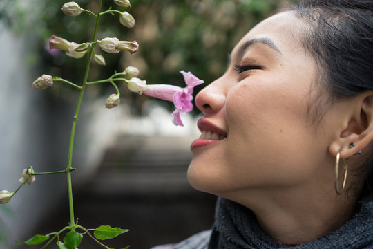 Closeup of crop Asian female on vacation smiling while enjoying smell of purple flower with lane on blurred background at Albaicin in Granada