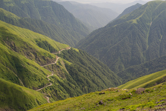 From above amazing view of empty serpentine road on green grassy hillside against misty valley and forested mountains in Georgia