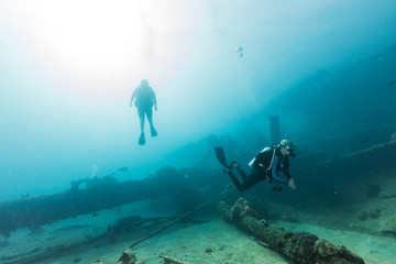 Divers researching bottom with submerged ship mast fragments in transparent ocean