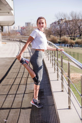 Young athletic woman in a white t-shirt and gray leggings before a workout in the fresh air does a workout.