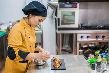Side view of serious young female chef garnishing and finishing gourmet dish ready for serving while working at table in restaurant kitchen