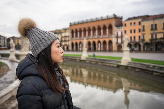 Side view of young Asian resting lady in warm clothing and hat walking at beautiful Prato della Valle park at Padova at Italy 