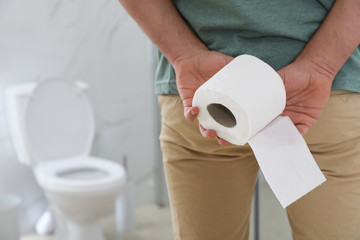 Man with toilet paper suffering from hemorrhoid in rest room, closeup