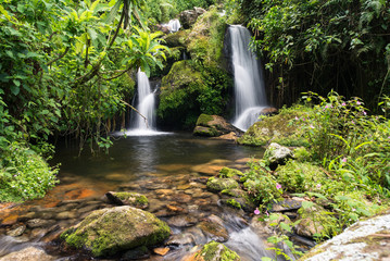Uganda - November 26, 2016: Wonderful scenery of mountain river cascade flowing into pond with rocky bottom among green jungle thickets in hot sunny day