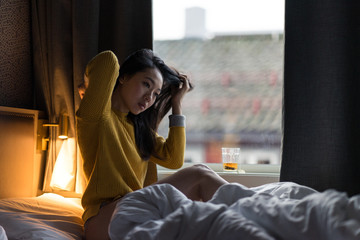 Asian woman in yellow sweater sitting on bed near window on lazy morning at Tromso in Norway