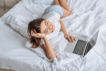 cheerful woman using laptop while chilling in bedroom