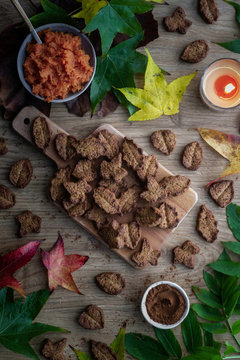 Top view of tasty biscuits and autumn leaves placed on wooden table near cocoa powder and sweet paste