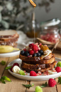 Liquid honey spilling on stack of fresh toast with fresh berries and mint during breakfast on table