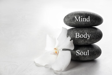 Stones with words MIND, BODY, SOUL and orchid flower on light background. Zen lifestyle