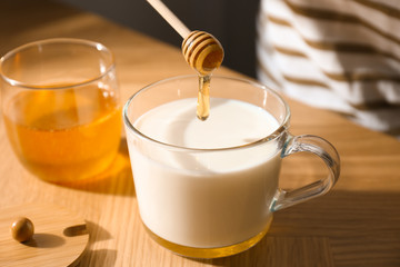 Adding honey to milk at wooden table, closeup