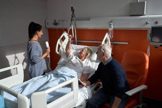 Adult woman and senior man visiting recovering mature female patient in modern ward of hospital