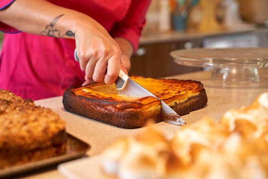 Crop anonymous woman in vivid pink clothes cutting with knife pie baked with tasty crust while standing at table and finishing cooking pastry at home