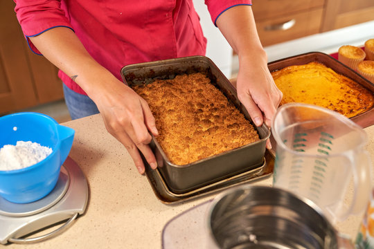 High angle of crop woman in colorful clothes taking out ready tasty pie brown crust with from rectangular baking tray after preparing in oven at home