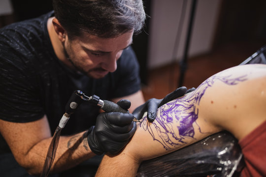 Master doing tattoo on forearm of male customer