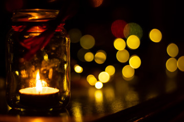 A small candle burns in a jar in the dark against the background of bokeh lights