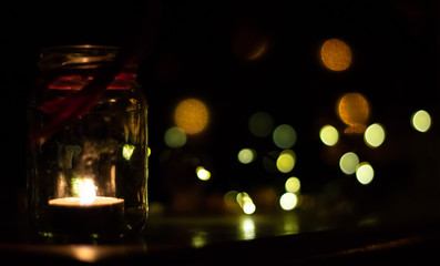 A small candle burns in a jar in the dark against the background of bokeh lights