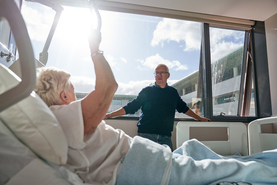 Senior male visitor standing near window and speaking with female patient in ward of modern hospital
