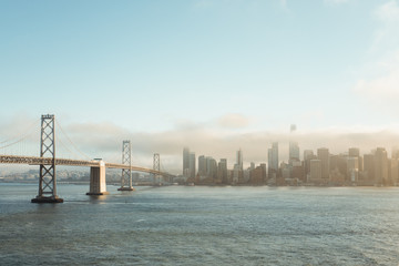 Metal bridge stretching to downtown in cloudy haze above water in San Francisco