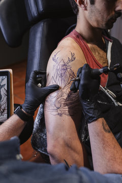 Master doing tattoo on forearm of male customer