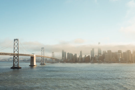 Fototapeta Metal bridge stretching to downtown in cloudy haze above water in San Francisco