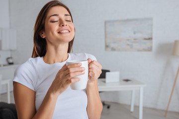 cheerful woman dreaming while holding cup of tea
