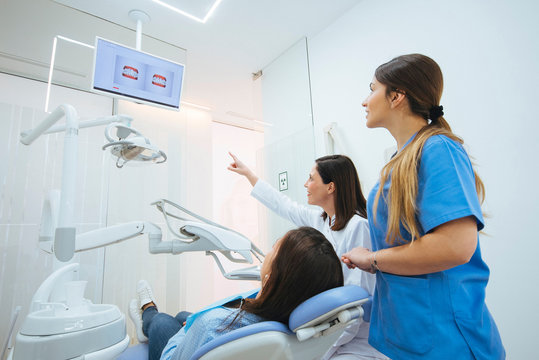 Dentist and assistant showing structure of teeth in picture to client in chair