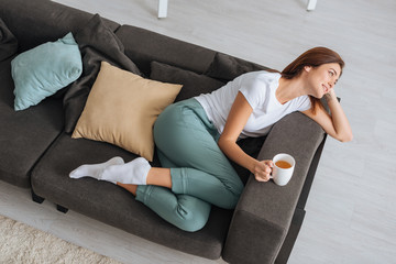 overhead view of attractive woman chilling of sofa with cup of tea
